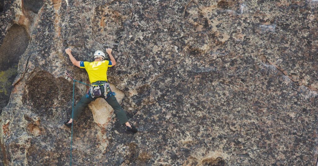 A climber in a helmet and safety gear scales a rough rock face in daylight.