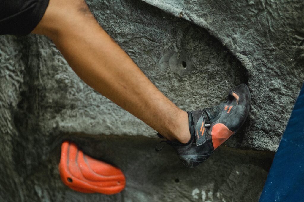 Crop unrecognizable male alpinist in sport sneakers practicing bouldering in modern climbing center