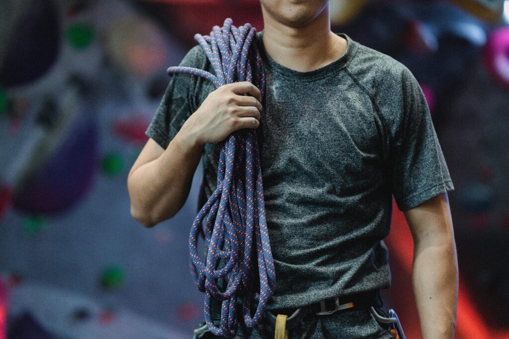 Crop unrecognizable male athlete in sportswear with belay and rope standing in bouldering center