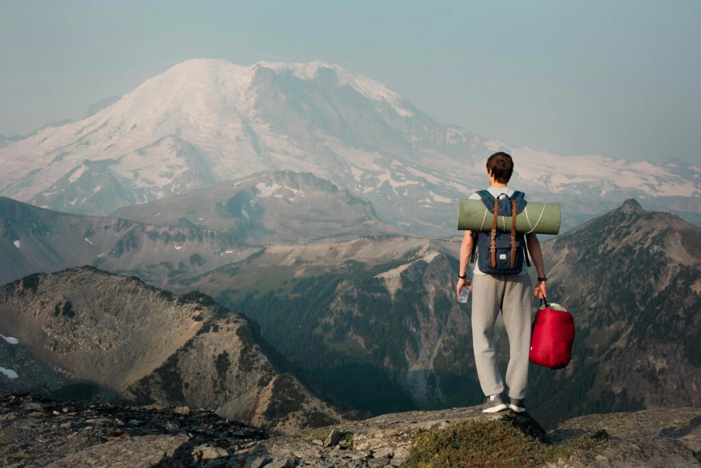 Backpacker on a mountain ridge gazing at a snow-covered peak, embracing adventure.