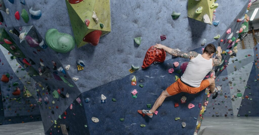 Tattooed man rock climbing on an indoor rock wall with colorful holds.